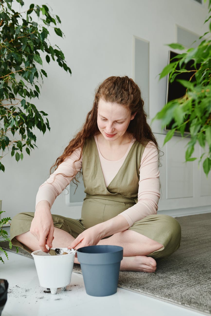 A pregnant woman sits indoors tending to potted plants, reflecting calm and serenity.