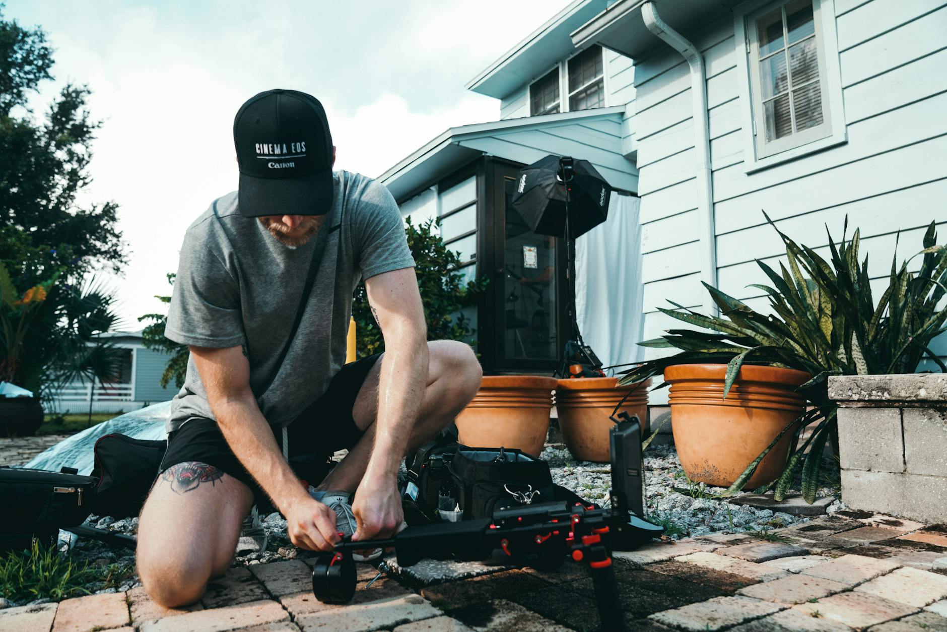 A man sets up film equipment in a home garden, focusing on camera gear outdoors.