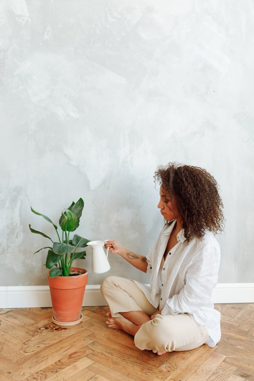 A young woman watering a potted plant in a stylish, minimalist room.