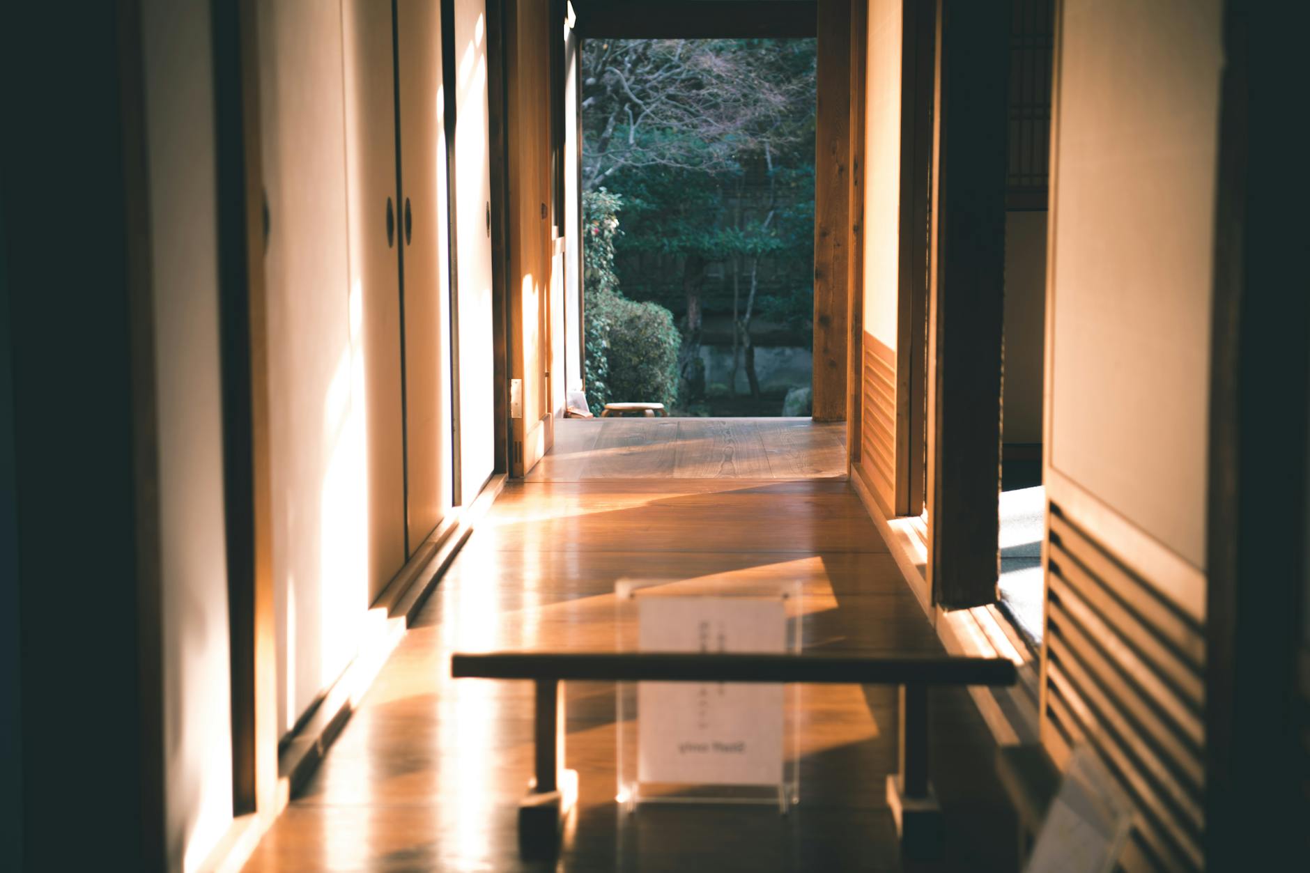 A tranquil Japanese interior hallway with wooden floors and sliding doors illuminated by sunlight.