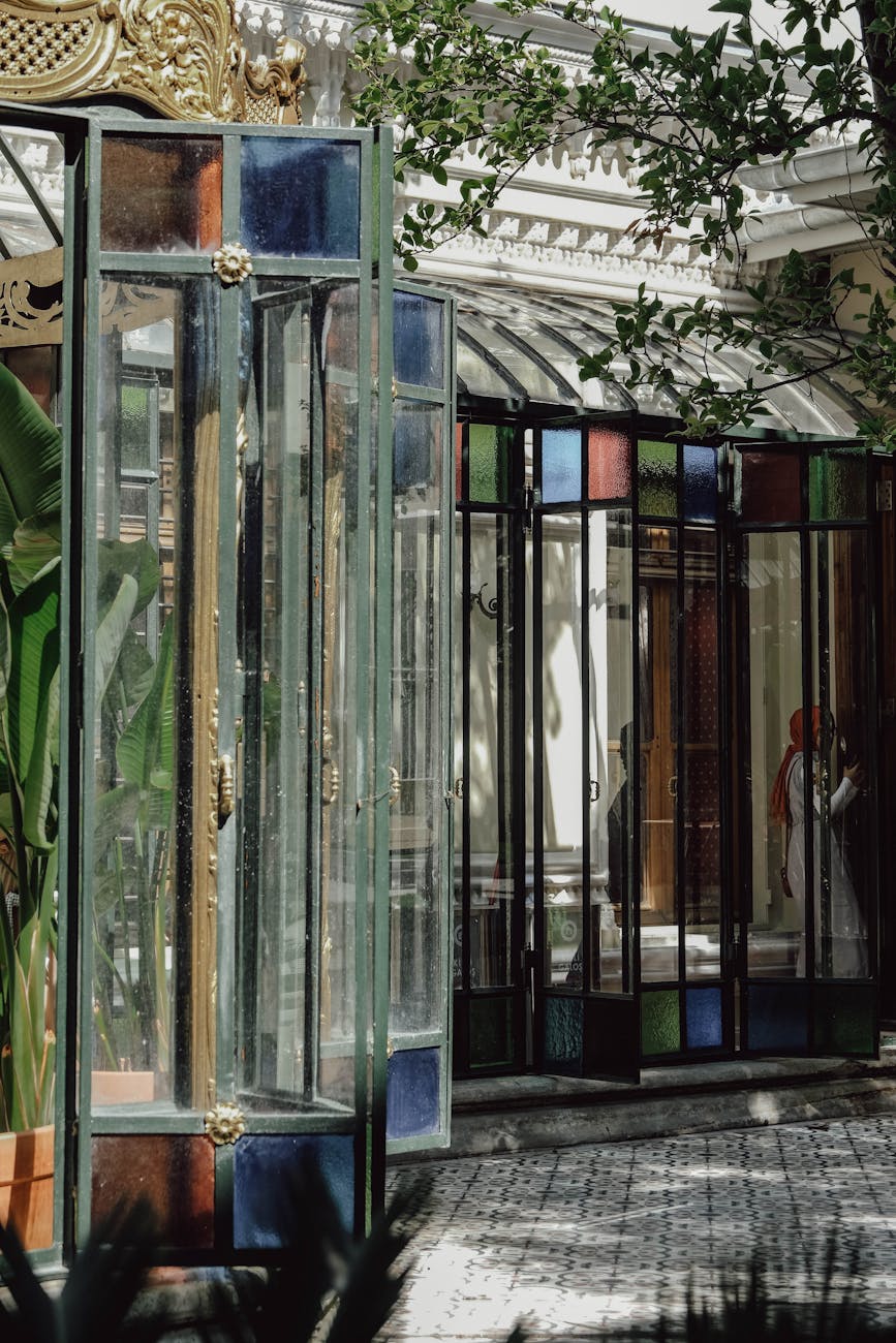 Sunlight through stained glass doors in historic conservatory, creating kaleidoscopic reflections.