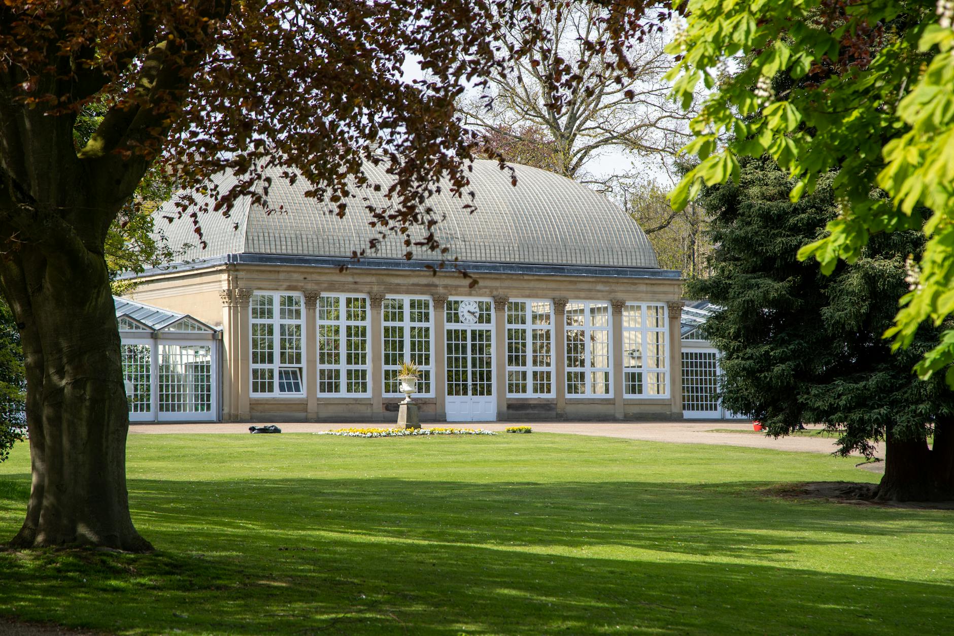 A beautifully clear view of a botanical garden dome surrounded by lush green trees and grass.
