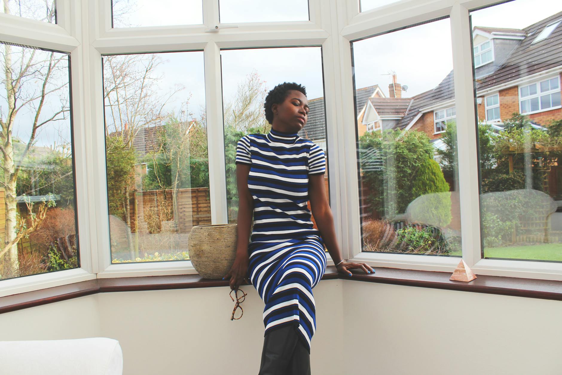 Stylish portrait of an elegant woman in a striped dress sitting by a window.