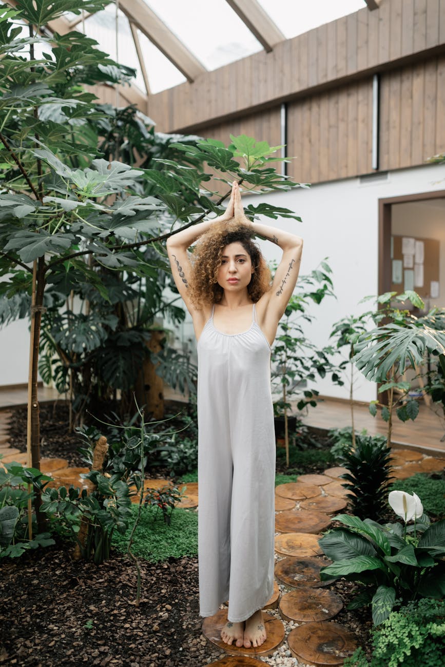 Adult woman with tattoos doing yoga pose in indoor garden.