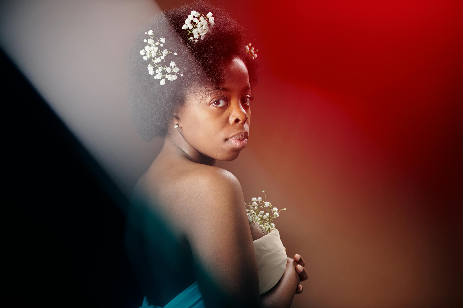 Elegant portrait of a young woman with afro hairstyle and floral accents, embodying natural beauty.