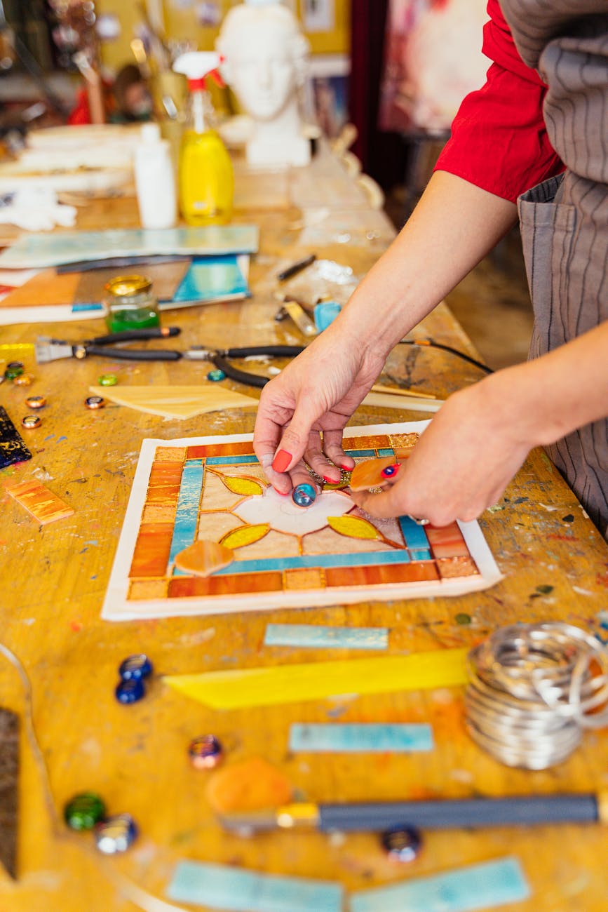 Close-up of artisan creating stained glass piece with colorful tools and materials on work table.